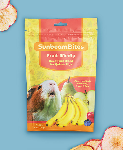 A yellow stand-up pouch labeled SunbeamBites Fruit Medley, Dried Fruit Blend for Guinea Pigs, featuring a guinea pig with bananas, an apple, blueberries, and a pear, set against a blue background with dried fruit slices.